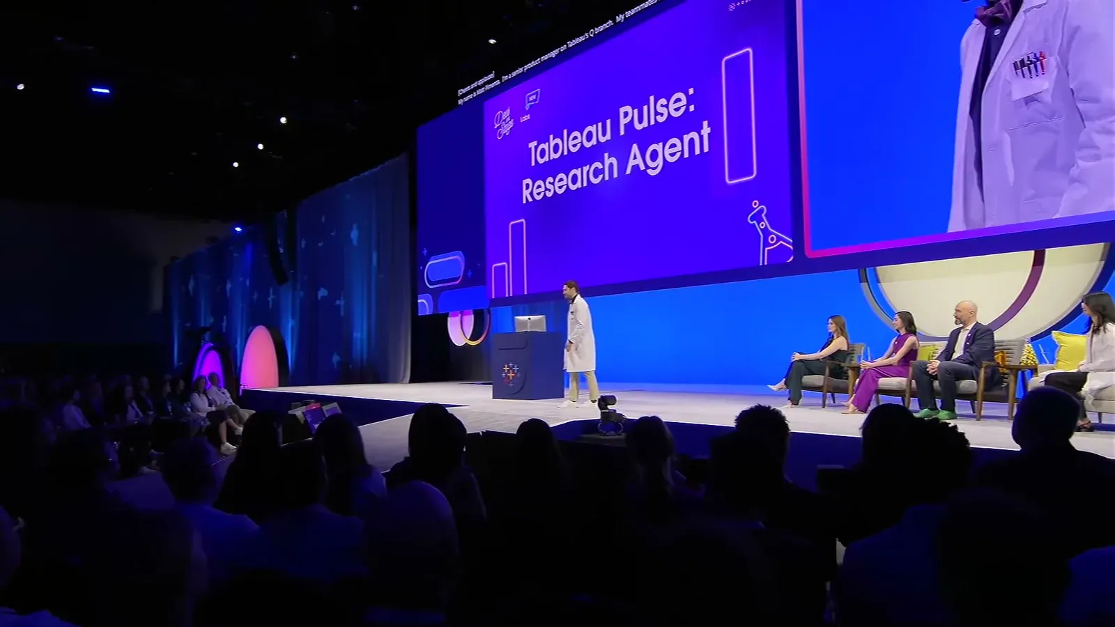 Matthew Pimenta onstage at Tableau Conference 2025, in a white lab coat beside a podium, with a screen behind him reading “Tableau Pulse: Research Agent” and the audience in the foreground.